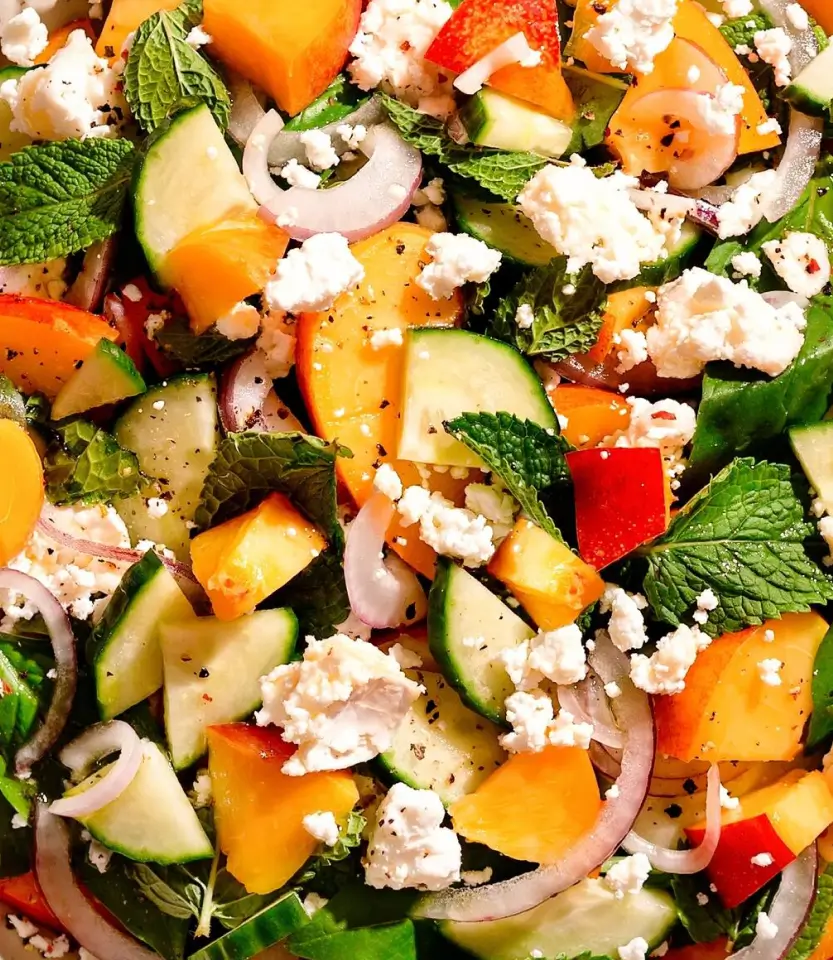 Colorful salad with diced cucumbers, bell peppers, red onions, feta cheese, fresh mint, and black pepper seasoning.