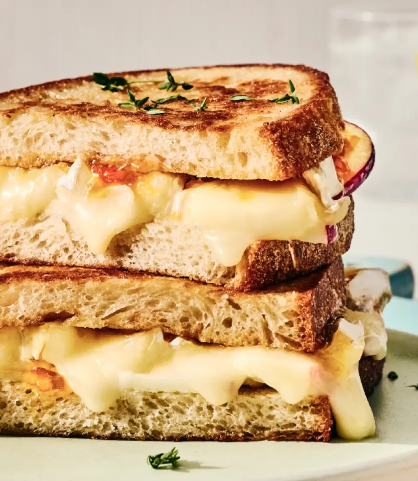 Stacked grilled cheese sandwiches with melted cheese and red onions on toasted bread, garnished with fresh herbs.