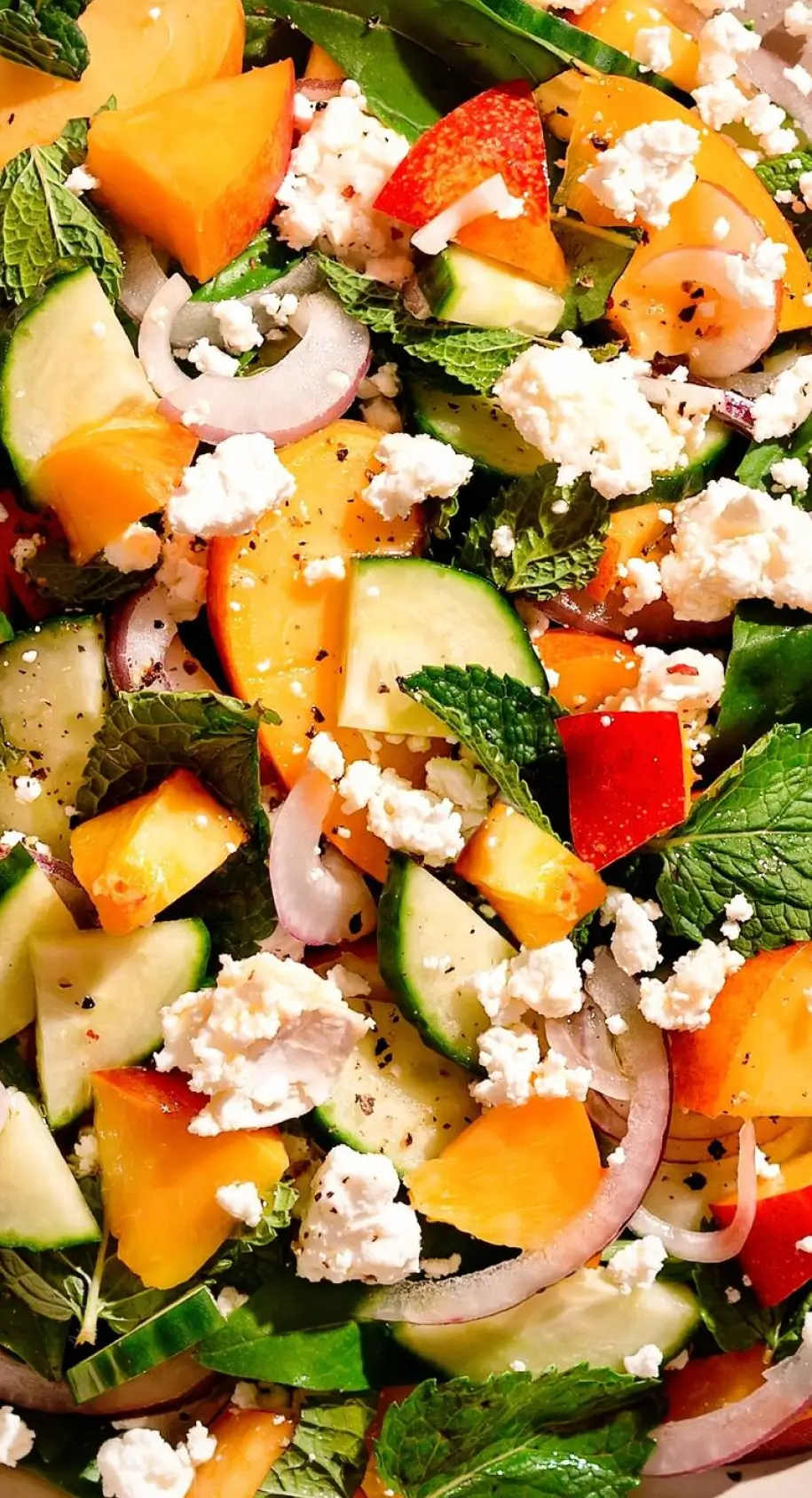 Colorful salad with diced cucumbers, bell peppers, red onions, fresh mint, crumbled feta cheese, and black pepper seasoning.
