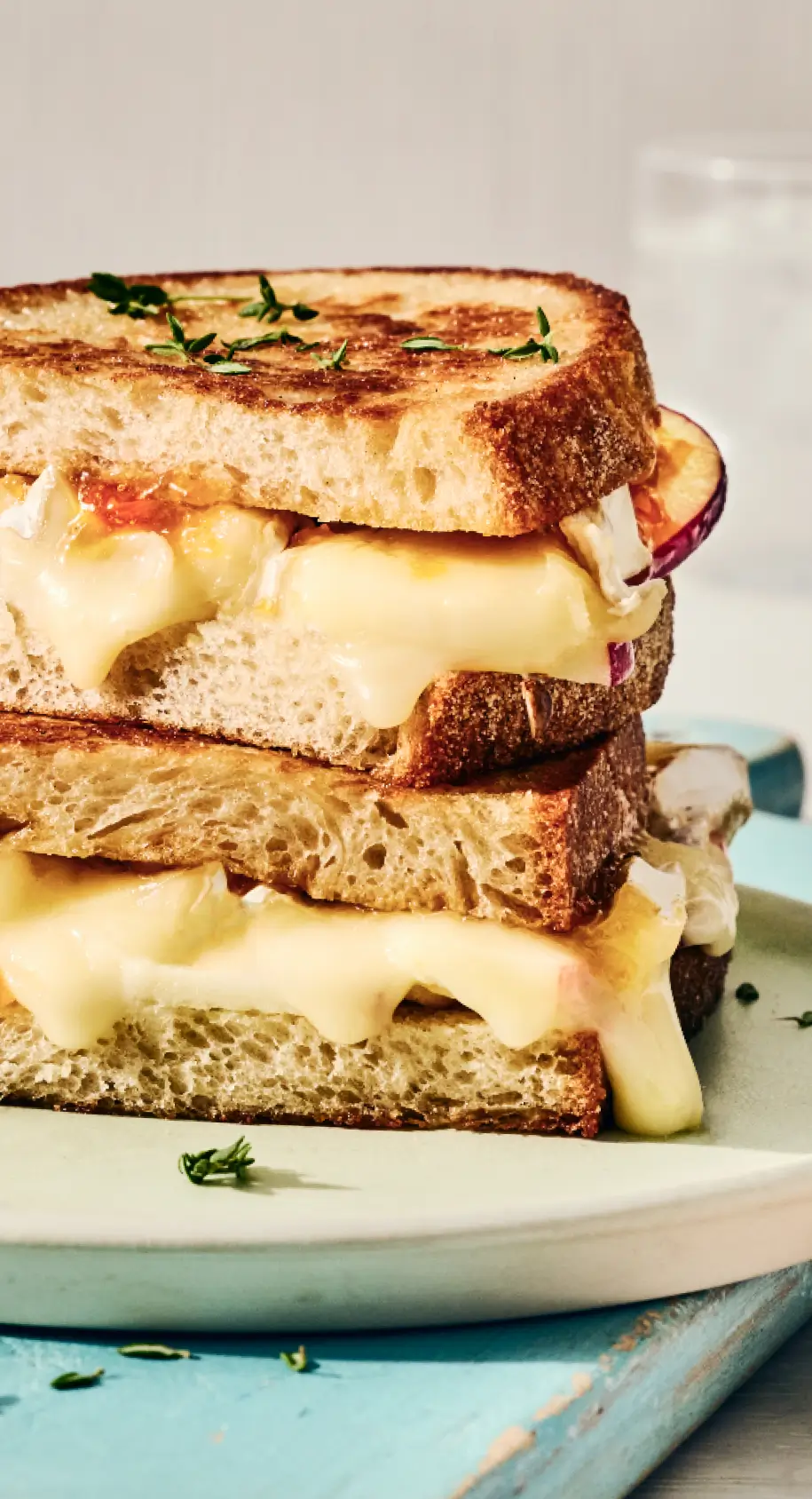 Stack of three grilled cheese sandwiches with melted cheese and red onion on toasted bread, garnished with fresh thyme on a white plate.